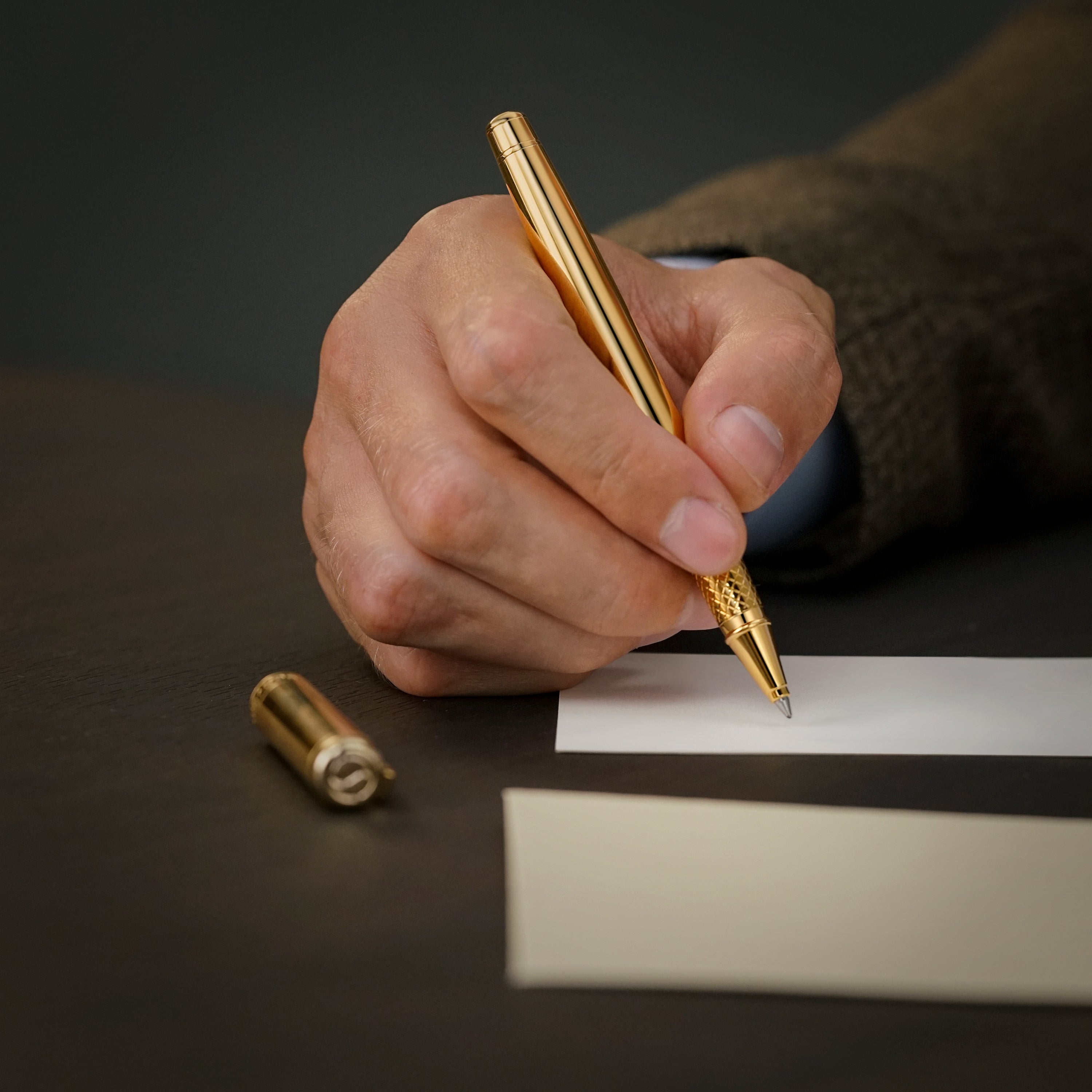 Hand holding a gold pen about to write on a piece of paper with a dark background
