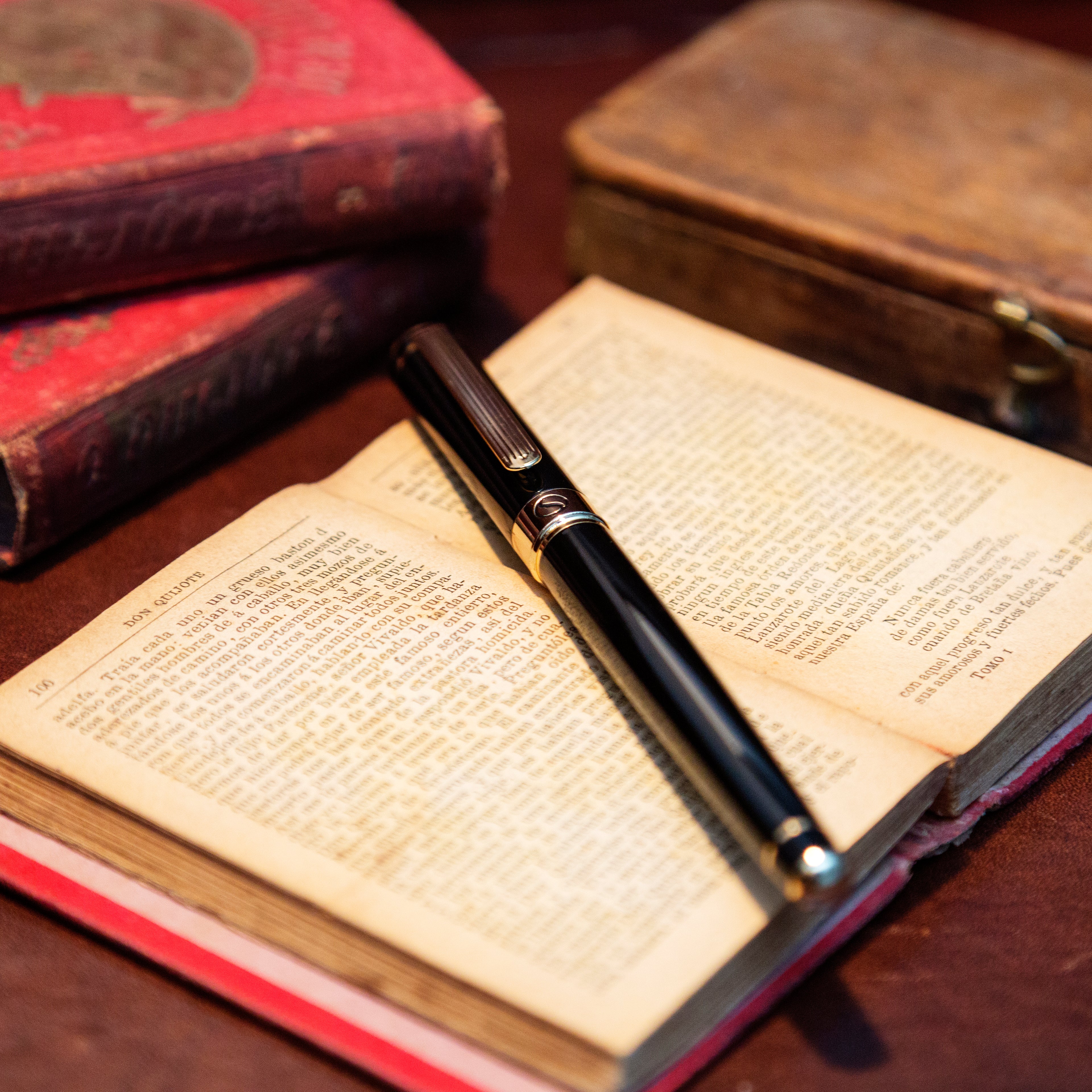 Open book with a pen on top, surrounded by vintage books on a wooden surface